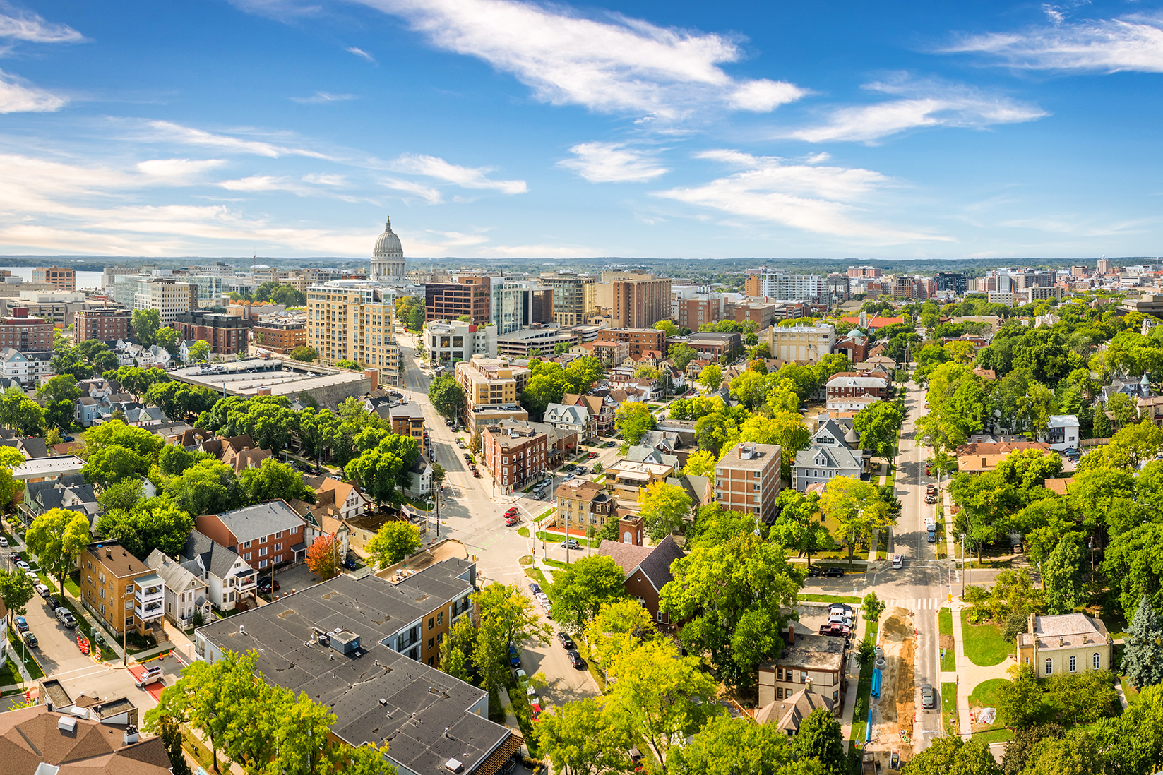 Aerial cityscape with a domed capitol building, mid-rise and low-rise buildings, and tree-lined streets.