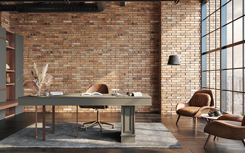 Modern office with a brick wall, large window, and a dark desk accompanied by a brown leather chair and a floor lamp.